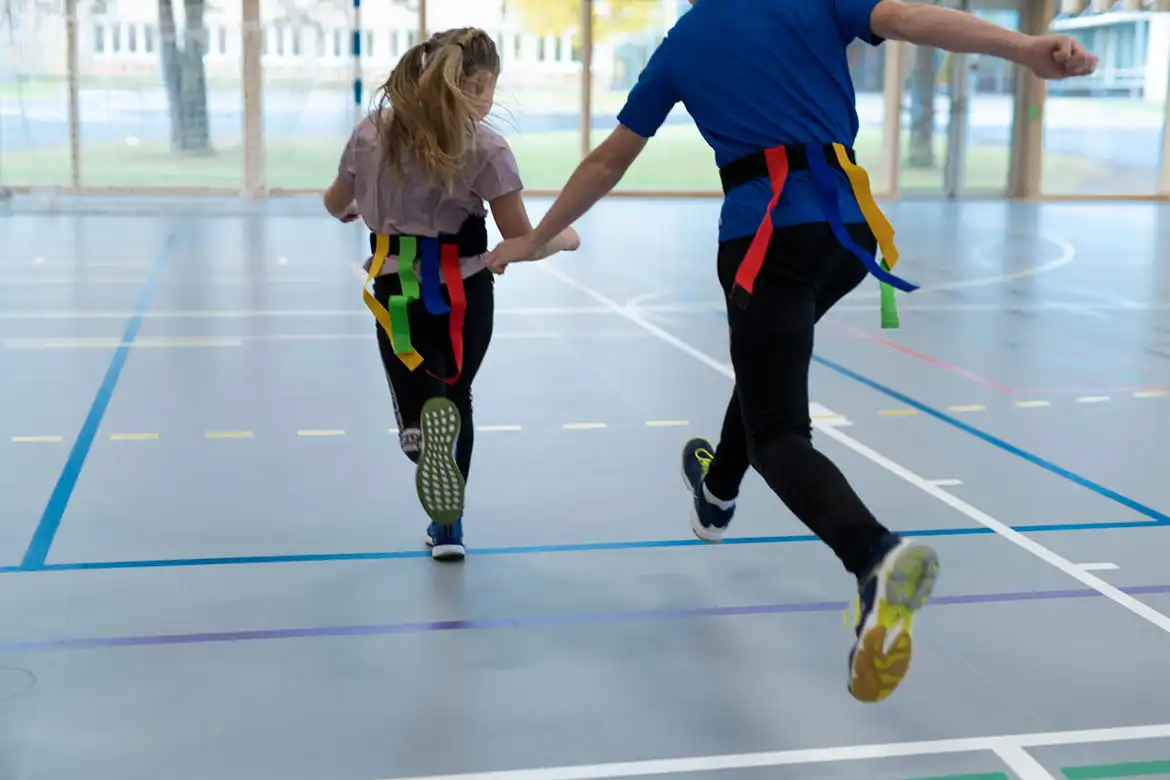 En skoleklasse leker nappehale lek innendørs i gymsalen