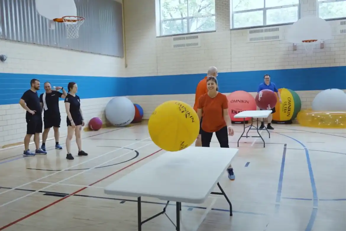 En gruppe mennesker spiller Omnikin Table Ball innendørs i en gymsal