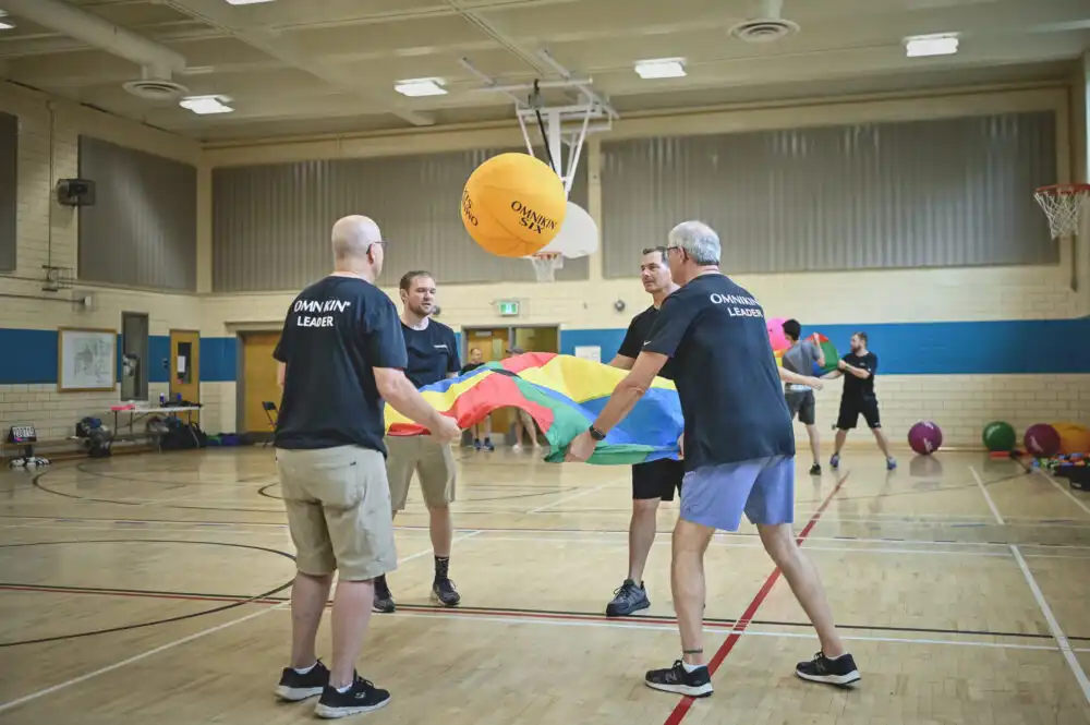 En gruppe mennesker leker leken Omnikin Parachute Hijinks