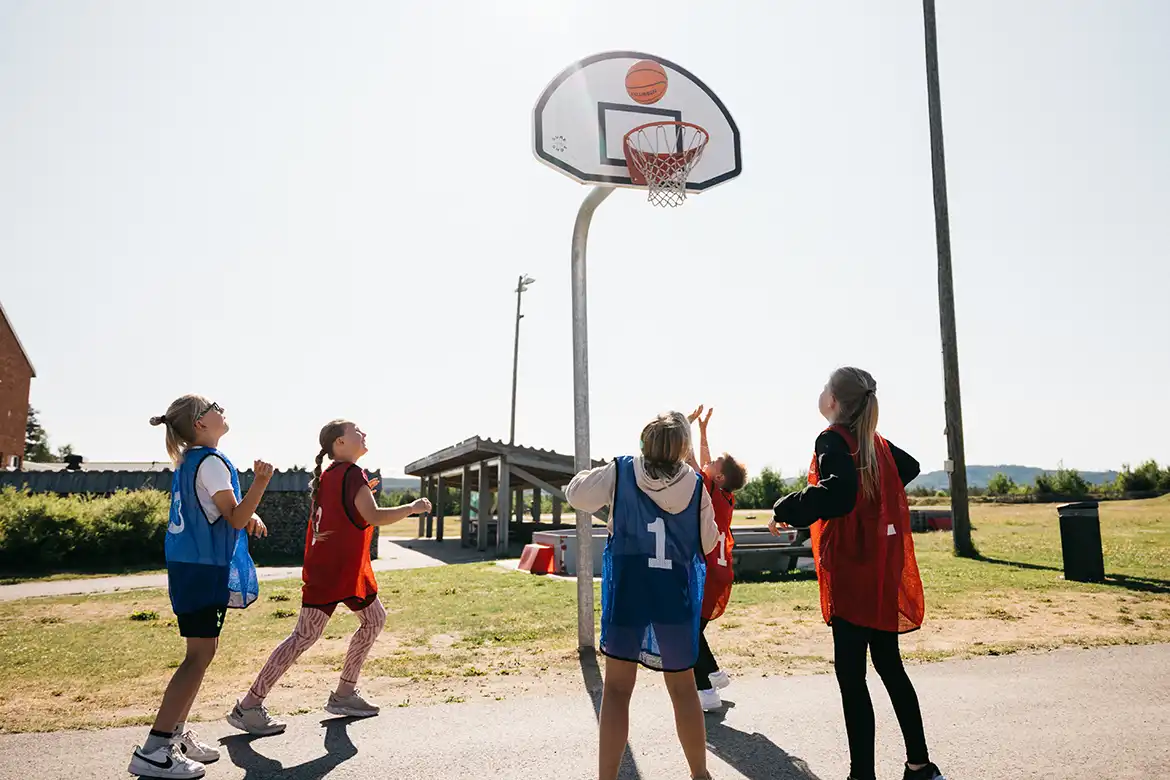 Barn som spiller basketball ute i skolegården